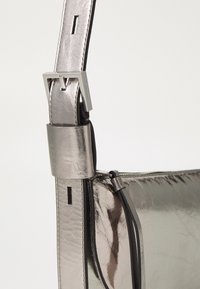 Metalická stříbrná taška přes rameno s hladkým povrchem, nastavitelným popruhem se stříbrnou sponou a elegantním designem s minimem doplňků.