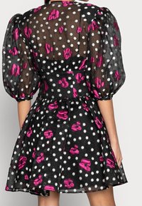 Robe noire en tissu transparent, à pois et accents floraux roses. Elle présente des manches bouffantes et une jupe évasée.