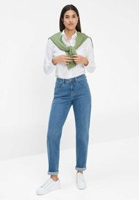 Helles blaues Denimjeans mit geradem Bein, hochgekrempelten Säumen und zwei vorderen Taschen, kombiniert mit einem weißen Hemd und einem grünem Pullover, der um den Hals gebunden ist.