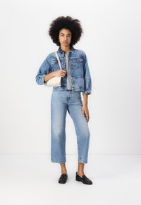 Casaco de ganga e jeans azuis, ambos com lavagem clara, combinados com uma blusa cinza. Sapatilhas pretas sem atacadores e uma pequena mala branca de ombro.