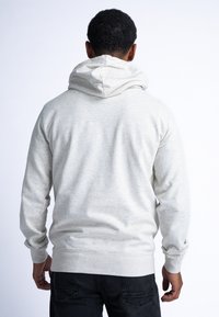 Sudadera gris claro con una textura suave, que presenta una capucha con cordones y puños acanalados. Diseño simplista sin logotipos visibles.