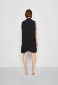 Svart ärmlös klänning med hög krage, flödande silhuett och medlång längd. Tillverkad av ett mjukt, lätt tyg.