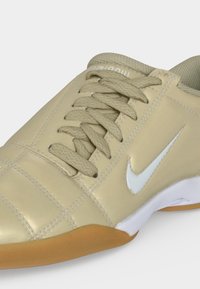 Κοντινή λήψη μπεζ αθλητικού παπουτσιού Nike με ανάγλυφα κορδόνια, λευκό λογότυπο swoosh και σόλα χρώματος καουτσούκ σε φωτεινό φόντο.