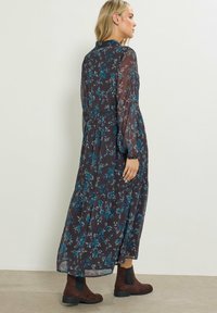 Abito fluido a maniche lunghe in tessuto scuro con motivo floreale blu. Presenta una gonna a balze ed è abbinato a stivali alla caviglia marroni.