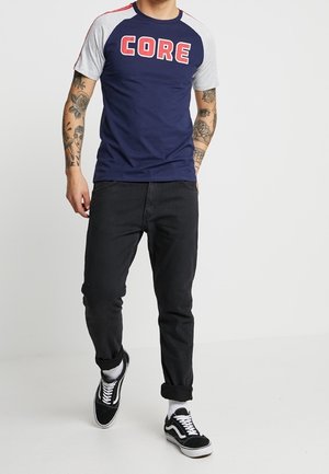 T-paita tummansinisenä, harmailla raglan-hihoilla, jossa on rohkeaa punaista "CORE" -tekstiä. Yhdistetty mustiin farkkuihin ja mustiin lenkkareihin.