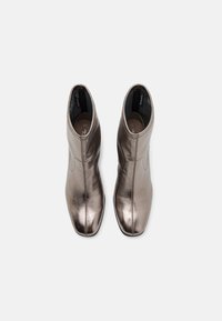 Paire de bottines en bronze métallique à bouts carrés et fermetures éclair latérales, vues de dessus sur fond blanc.