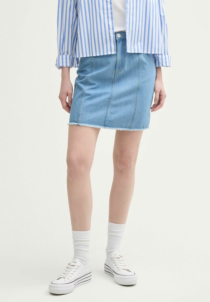 Lichtblauwe denim minirok met een rafelige zoom, rits en knoop, verticale naden, gecombineerd met witte sneakers en sokken.