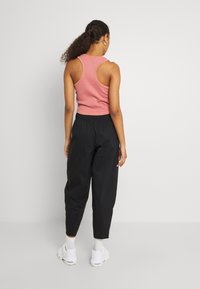 Figurformad rosa ribbad linne tillsammans med svarta, löst sittande byxor. Modellen står med ryggen vänd, vilket visar outfitens silhuett.