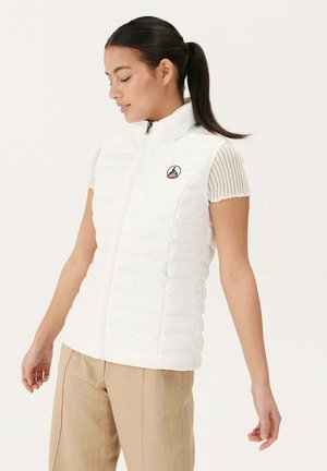 Chaleco acolchado blanco con cuello alto, cierre de cremallera y parche con el logo en el lado izquierdo del pecho, combinado con una camiseta de manga corta con canalé.