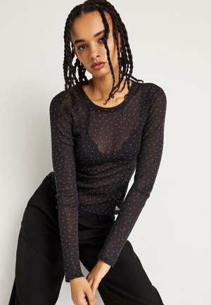 Maglietta nera a maniche lunghe realizzata in materiale trasparente, con un motivo a pois. Collo rotondo e vestibilità slim, abbinata a pantaloni neri larghi.