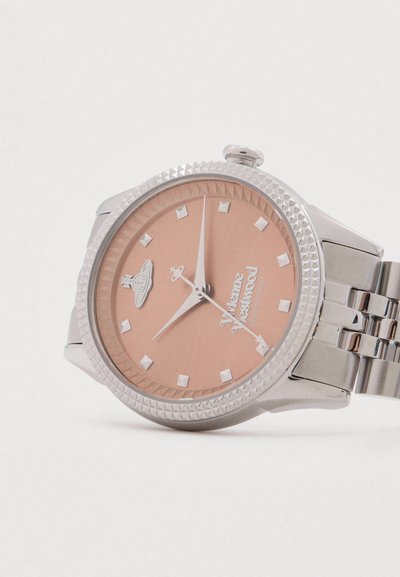 Sudraba metāla pulkstenis ar strukturētu rāmi, rozā ciparnīcu, dimanta stundas rādītājiem un Vivienne Westwood logotipu ar orb emblēmu pie pulksten 12.