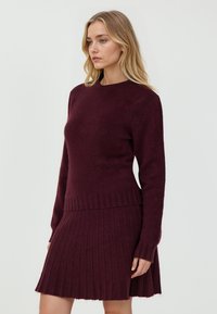 Bordeaux gestrickter Pullover und Plisseerock-Set. Weiche Textur, gerippte Details an den Bündchen und am Saum, taillierte Oberteil, ausgestellter und knielanger Rock.