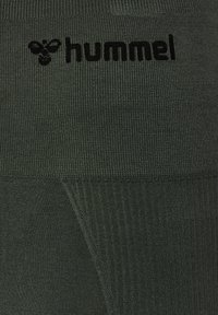 Leggings sportivi di colore verde scuro realizzati in tessuto testurizzato, con un logo "hummel" nero nella parte superiore.
