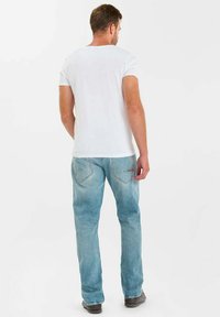 T-shirt blanc à manches courtes et jean en denim bleu clair. Le jean comporte des poches arrière avec des coutures discrètes. Design simple, coupe décontractée.