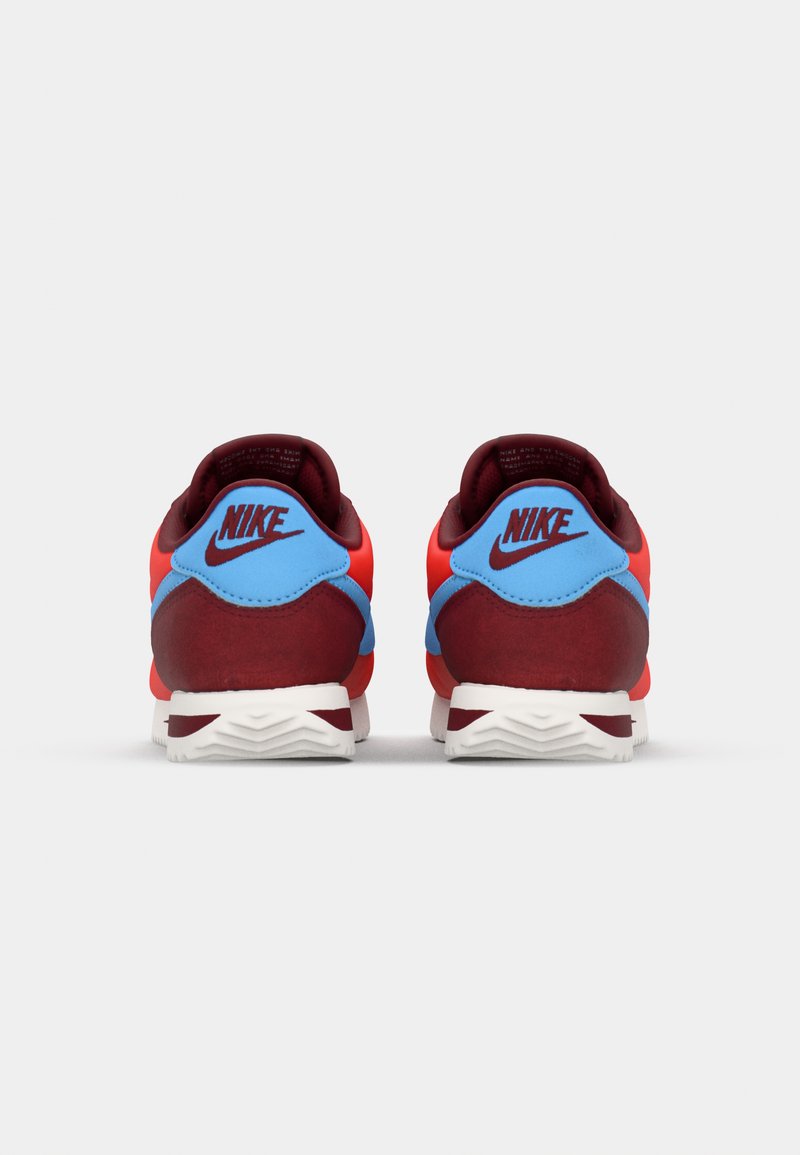 Zapatillas Nike con una combinación de colores rojo y azul, presentando una parte superior de textura suave y una suela blanca. La vista trasera destaca la ubicación del logo.