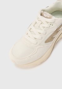 Baskets blanches avec un dessus en maille et en daim, présentant un profil texturé et un accent beige. Semelle épaisse offrant amorti et soutien.