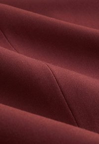 Bordó szövet, amely sima textúrát és finom fényességet mutat, ferde hajtással, amely kifinomult szövési mintázatot tár fel.