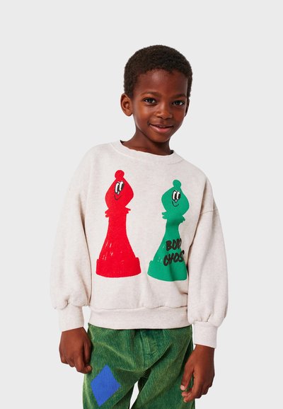 Felpa grigia chiara con grafiche di pezzi degli scacchi rossi e verdi, scollo tondo e polsini a costine; abbinata a pantaloni in corduroy verde.