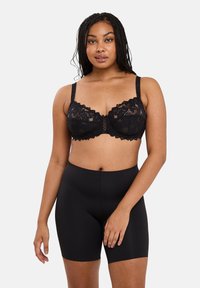 Soutien-gorge en dentelle noire avec des bords festonnés et un nœud central. Complété par un short taille haute noir, présentant une texture lisse et extensible.