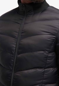 Giacca a vento nera con chiusura a zip, collo alto, design trapuntato e texture liscia. Leggera e aderente, adatta per il clima fresco.