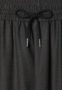 Cintura elástica negra con textura fruncida, que cuenta con un lazo de tela y extremos con punta metálica. Material suave y ligero.