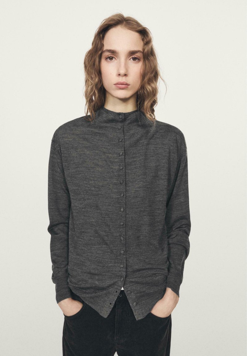 Camicia a maniche lunghe di colore grigio scuro con bottoni sul davanti, colletto alto e tessuto morbido, caratterizzata da una fila di bottoni e una vestibilità comoda.