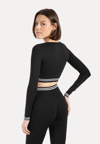 Czarny krótki top z długim rękawem, okrągłym dekoltem i paskiem w paski u dołu. Miękki, elastyczny materiał o dopasowanym kroju.