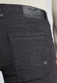 Jeans en denim noir avec un motif texturé subtil, dotés d'une étiquette en cuir portant la mention "PME Legend" et d'un design standard de poche arrière.