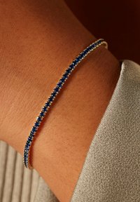 Silver bracelet adorned with blue gemstones, featuring a slim, round design that fits closely against the wrist. Smooth metallic finish.