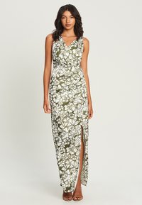 Maxi dress in white with green floral print, featuring a v-neck, fitted waist, and a thigh-high side slit. Smooth fabric with a flowing silhouette.