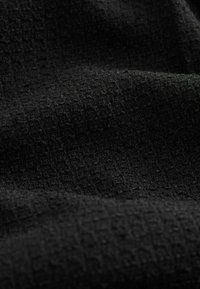 Tissu noir texturé avec un motif en grille subtil, présenté en gros plan avec des plis doux et des ombres.