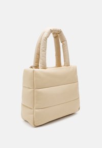 Beżowa torba na ramię z miękkim wypełnieniem, wyposażona w dwa zaokrąglone uchwyty, o wyraźnie zdefiniowanym, prostokątnym kształcie i poziomymi przeszyciami na przodzie.