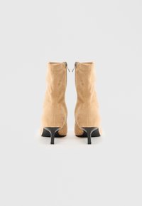 Et par beige semsket ankelstøvler med sorte kitten hæle og synlige bagte zippere på en hvid baggrund.