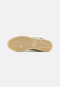 Sneaker outsole with a textured rubber surface, featuring a beige color and a zigzag pattern design for traction.