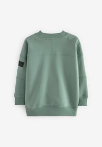 Grön sweatshirt med ribbad rundhals, långa ärmar och en strukturerad design. Har en svart tygetikett på vänster ärm.