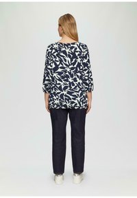 Langermige tuniek met een wit bloemenpatroon op een marineblauwe achtergrond, gecombineerd met donkere denim broek en zilveren sneakers. Glad textuur.