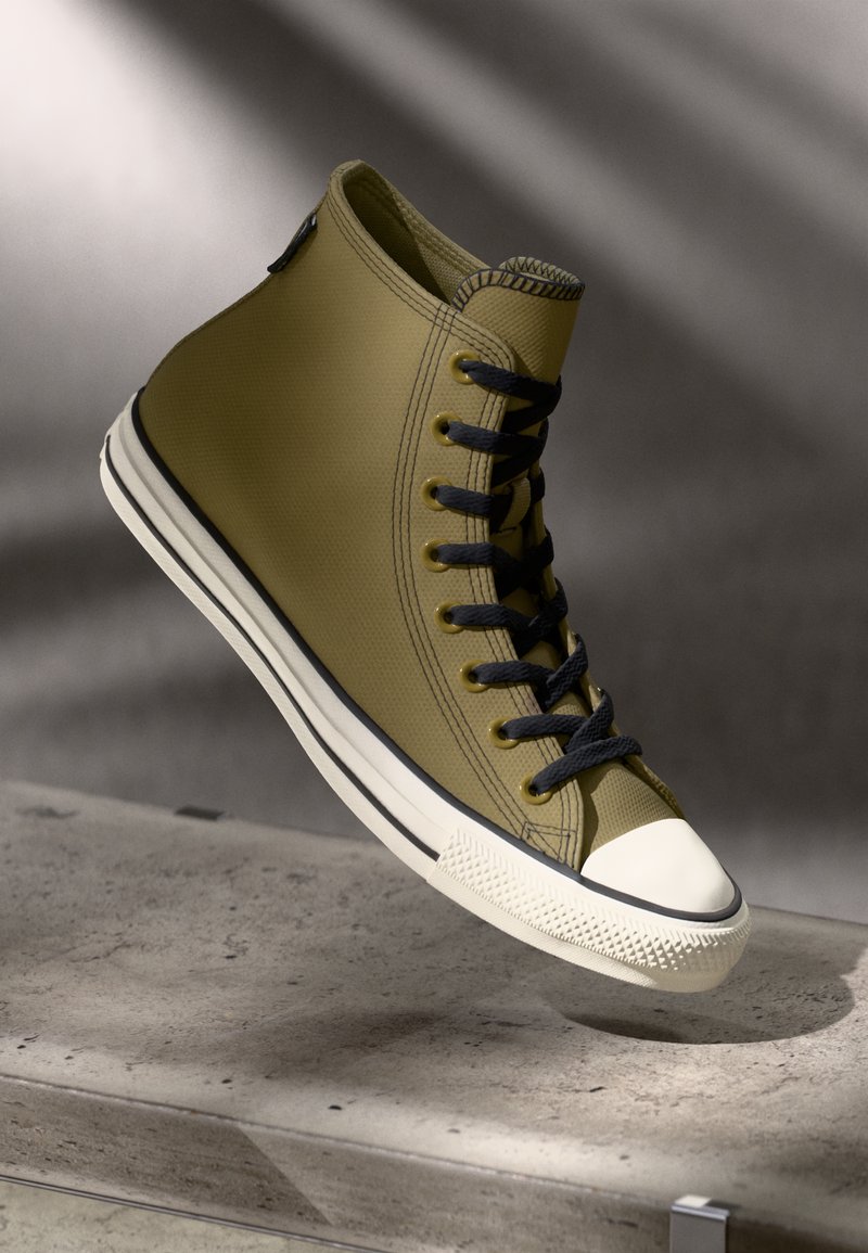 High-top sneaker in olive green, textured upper, black laces, white rubber toe cap, and contrasting white side stripe.