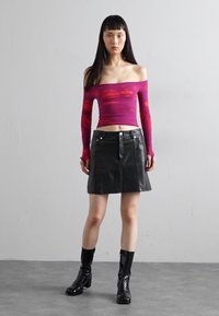 Purple long-sleeve top with red abstract patterns, paired with a black leather mini skirt. Model wears black ankle boots with a glossy finish.