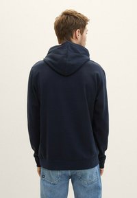 Granatowa bluza z kapturem z teksturowanej tkaniny, z dużym kapturem, prążkowanymi mankietami i dołem, w połączeniu z jasnoniebieskimi dżinsami.