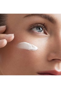 Nałożony na jasną skórę na policzku nawilżający krem, gładka, biała tekstura, miękka skóra, zbliżenie na oko i dłoń.