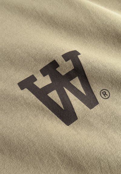 Tissu kaki avec une texture douce, présentant un design de logo audacieux et marron foncé en forme de "W" stylisé et un symbole de marque déposée.