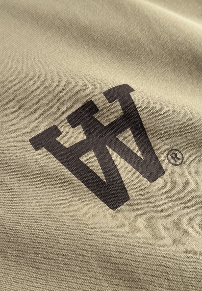 Tejido caqui con una textura suave que presenta un atrevido diseño de logo en marrón oscuro en forma de una 'W' estilizada y un símbolo de marca registrada.