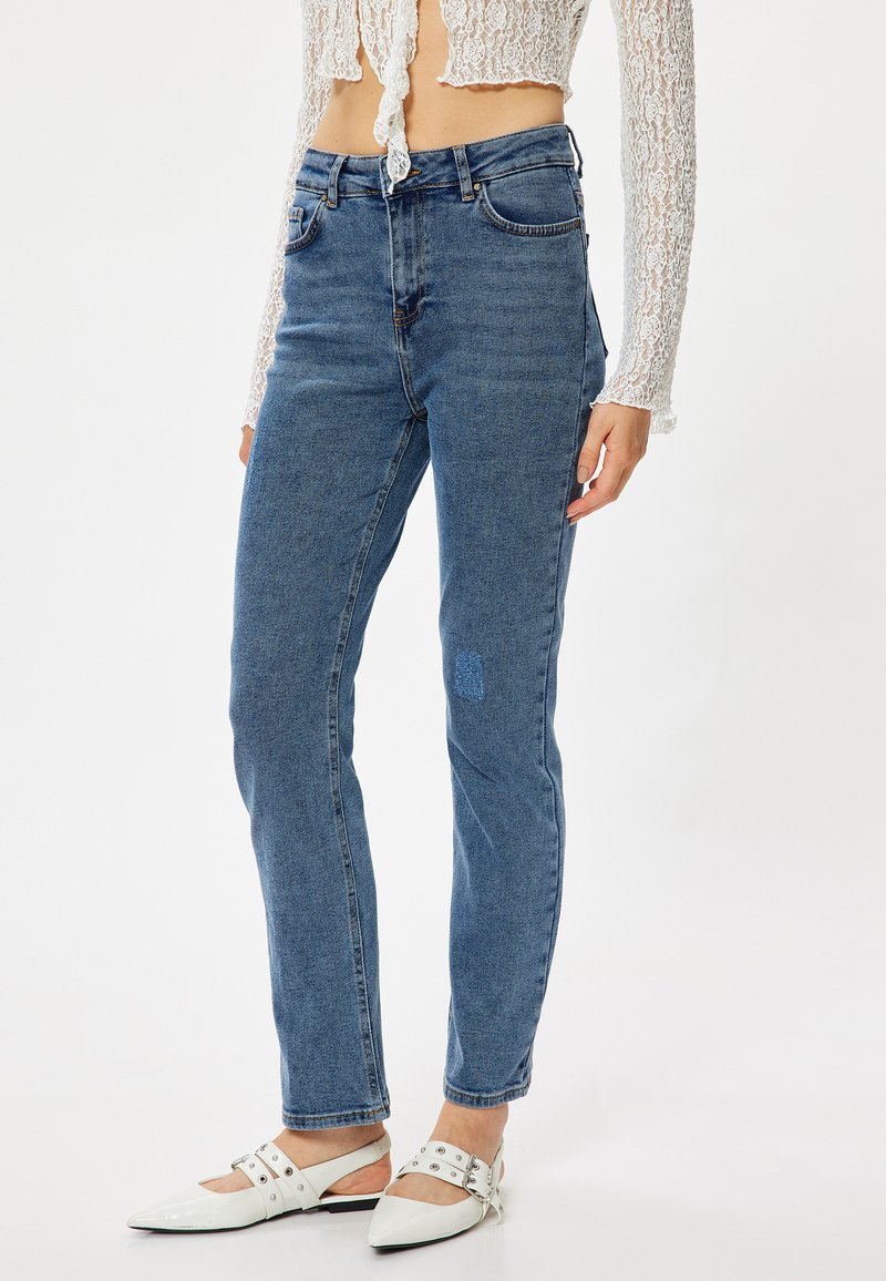 Jeans de mezclilla azules de tiro alto con un corte recto, que presentan un detalle de parche en el muslo izquierdo y un diseño tradicional de cinco bolsillos.