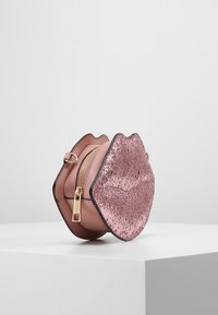 Pyöreä vaaleanpunainen nahkakotelo, joka on muotoiltu huulien mukaan, ja siinä on tekstuuri, kiiltävä vaaleanpunainen päällinen, kultainen vetoketju ja musta reuna.