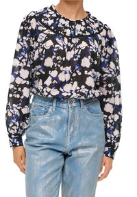 Blumenbluse mit einem schwarz-blau-weißen Muster, gerafftem Ausschnitt und langen Ärmeln. Kombiniert mit hellblauen glänzenden Jeans.