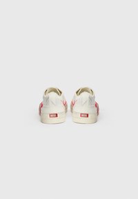 Weiße Leinenschuhe mit rotem Logo und Akzenten aus roten Nähten, ausgestattet mit einem Vintage-Design und beigen Gummisohlen. Verstärktes Fersen-Detail.