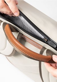 Borsa grigia con manico in pelle e zip nera. L'interno presenta una fodera in rete. Una mano sta tirando la zip verso il basso.