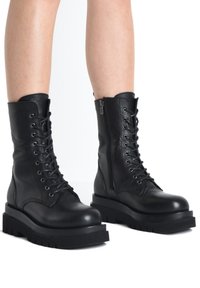 Černé kožené šněrovací bojové boty se bočním zipem, robustní gumovou podrážkou, zaoblenou špičkou a texturovaným svrškem.