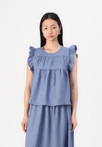 Top in misto lino blu chiaro con maniche a balze, scollo rotondo e design a strati. Tessuto testurizzato con un morbido caduta, abbinato a una gonna coordinata.