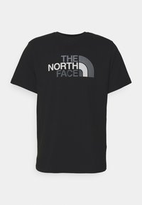 Mustan puuvillaisen T-paidan lyhyet hihat, joissa on suuri harmaa ja valkoinen logo, jossa lukee "THE NORTH FACE" rohkeassa muotoilussa.